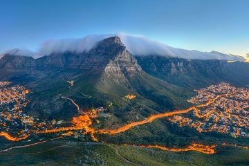 Table Mountain looms over Cape Town on Africa's southwest coast, its peaks swaddled in clouds as lights blaze in the city below.