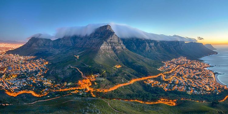 Table Mountain looms over Cape Town on Africa's southwest coast, its peaks swaddled in clouds as lights blaze in the city below.