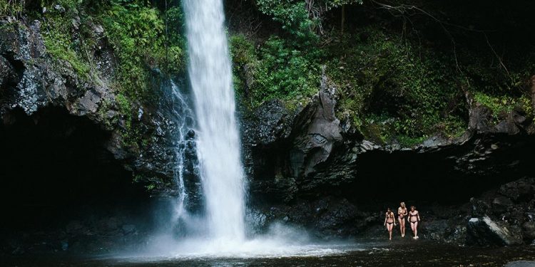 Three women in bathing suits standing by a waterfall.