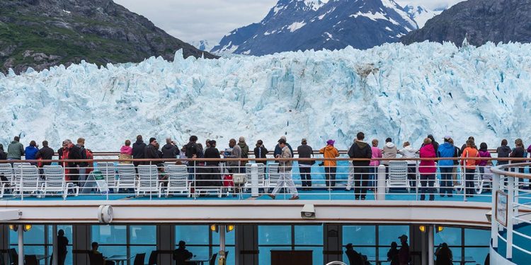 Tourists stand on deck of cruise ship to look at passing glacier.
