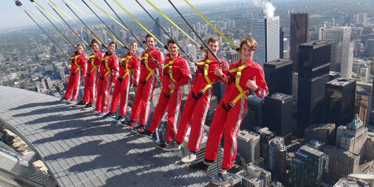 People in red jumpsuits and harnesses leaning over edge of Toronto skyline.