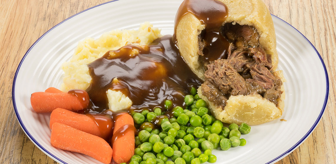 Steak and kidney pudding, peas, carrots, mashed potatoes and gravy on a plate