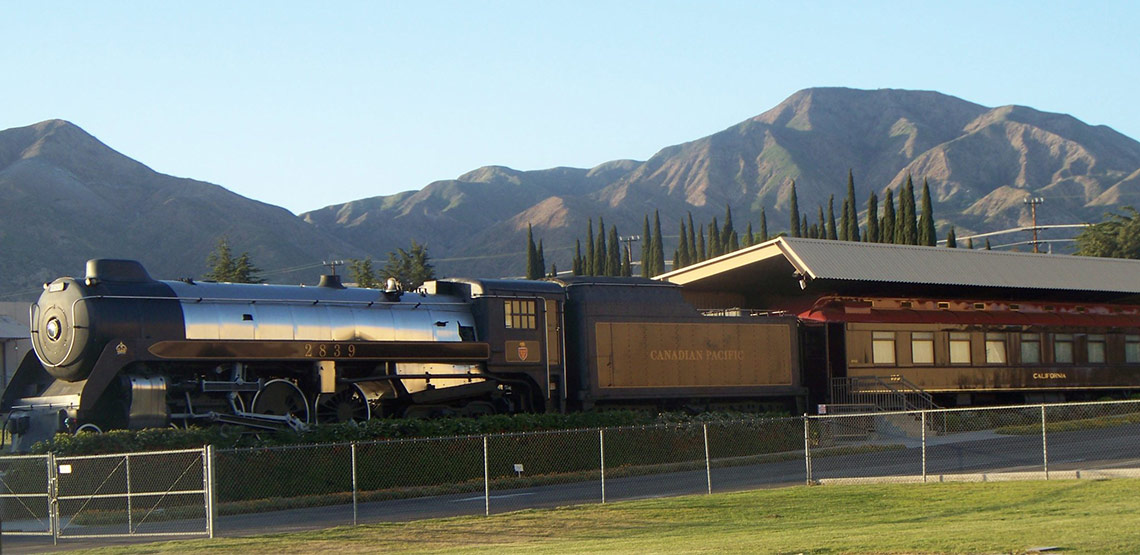 Royal Hudson steam train at a station with mountains in background.