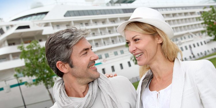 mature couple smiling at each other in front of a cruise ship