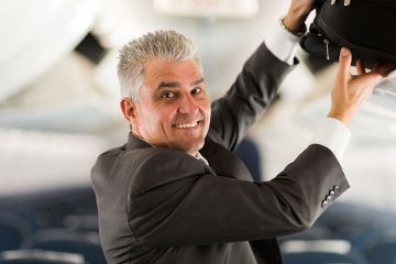 older man putting carry on in the overhead bin of an airplane