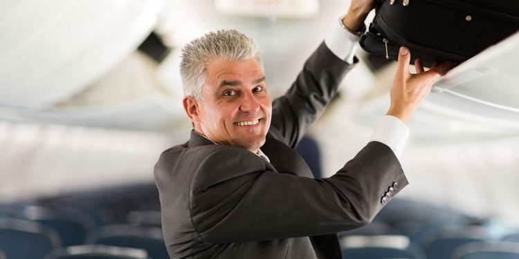 older man putting carry on in the overhead bin of an airplane