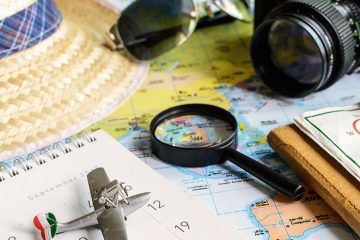 camera, sunglasses, a hat and other travel items sit on top of a map