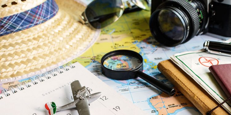 camera, sunglasses, a hat and other travel items sit on top of a map