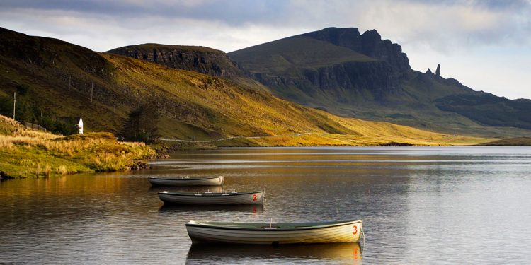 row boats tied to the shore with green Scottish cliffs in the background