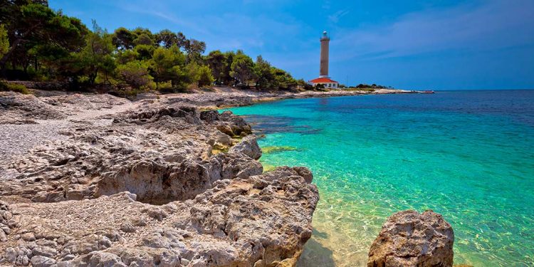 Turquoise waters on rocky coastline with lighthouse in distance.