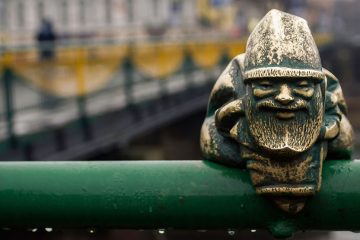 small metal gnome sculpture sits on a railing