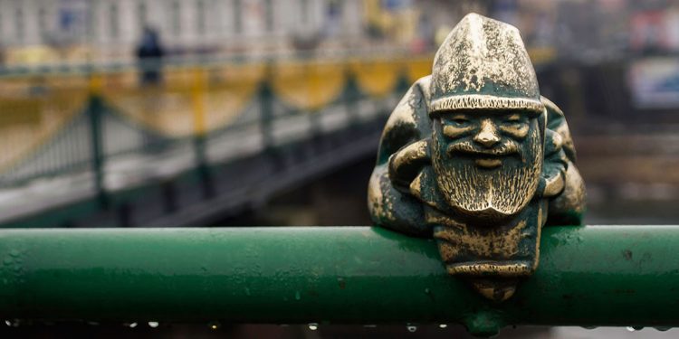 small metal gnome sculpture sits on a railing