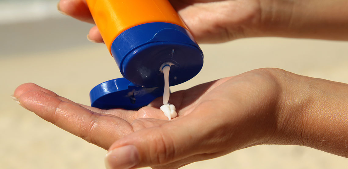 Sunscreen being poured into person's hand at the beach.