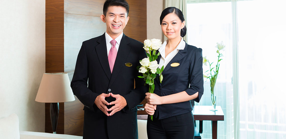 Two hotel staff pleasantly smiling with flowers