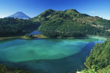 Dieng Plateau, blue lake set among green hills.