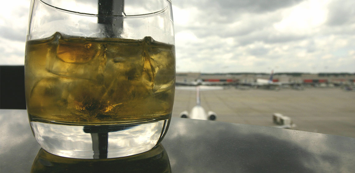 A mixed drink is on a table with a view of an airport runway
