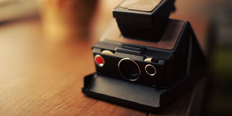 A polaroid camera sits on a wooden table.