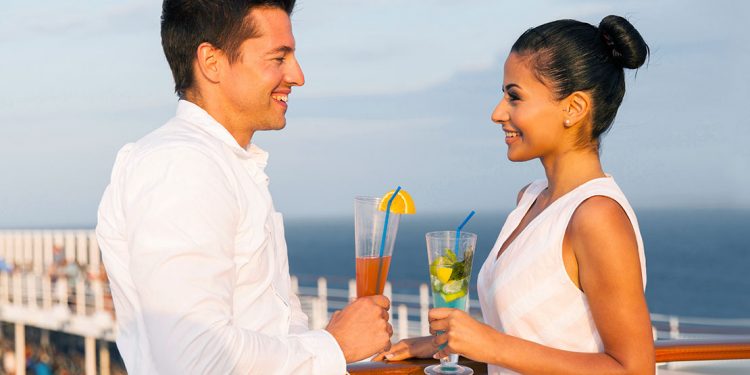 A man and woman look into each others' eyes while enjoying a cocktail on a cruise ship