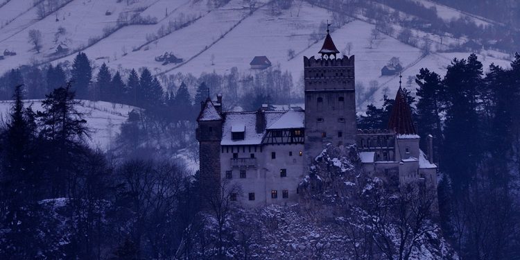 Perched atop a craggy rock, set against dark and imposing hills, Dracula's castle is seen in the dead of winter.