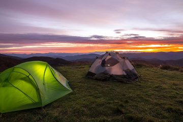 Two tents on rolling mountains during sunset.