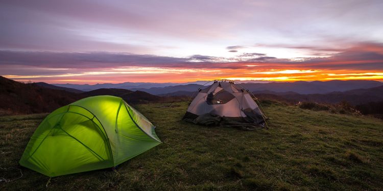 Two tents on rolling mountains during sunset.