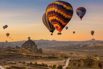 Sunrise over Cappadocia, Turkey with many hot air balloons hovering above the land.