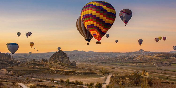 Sunrise over Cappadocia, Turkey with many hot air balloons hovering above the land.