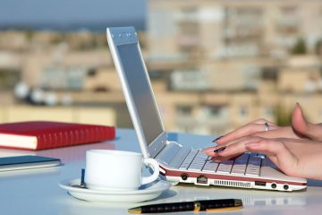 Female hands typing on laptop while sipping a coffee in foreign destination