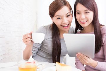 Two smiling women sitting at a cafe table look at an iPad