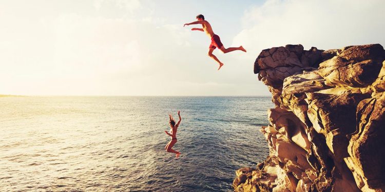 people jumping off a cliff into water