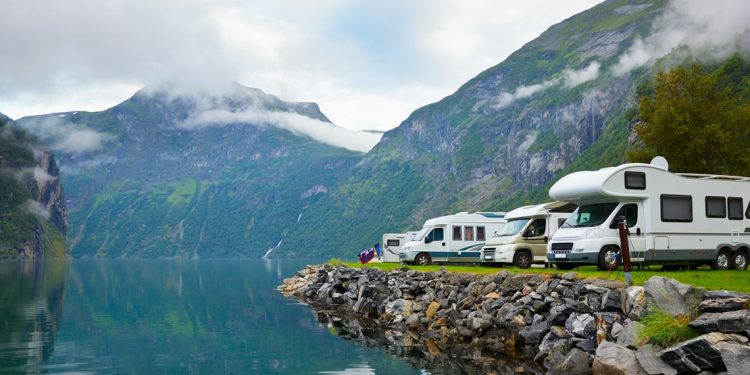 camper vans and rvs on a shoreline surrounded by green mountains