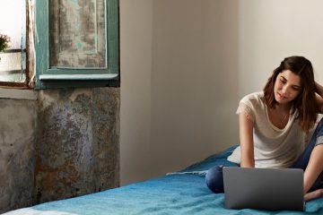 woman sitting on bed by window with laptop