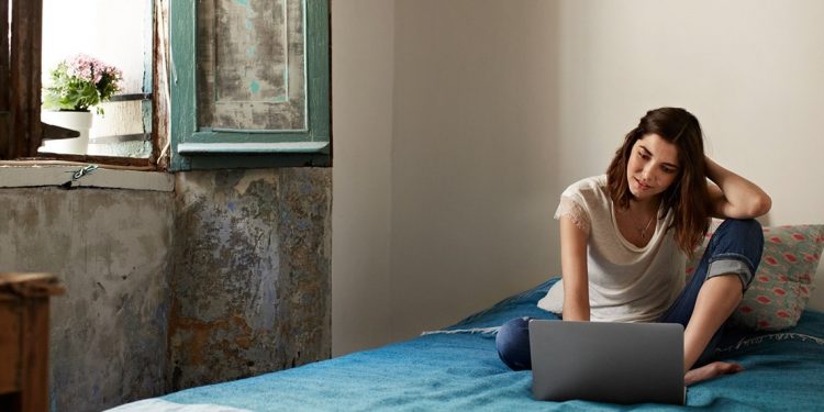 woman sitting on bed by window with laptop