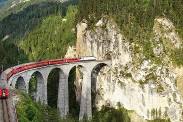 train crossing a large bridge surrounded by tree-covered mountains