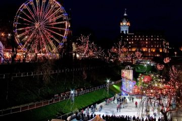 trees covered in christmas lights while patrons skate on ice rink at night in edinburgh, scotland