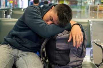 man napping against luggage in airport