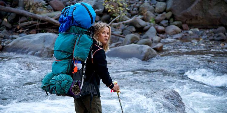 blonde woman crossing rushing river with large backpack
