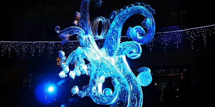 Ornate ice sculpture lit up with blue light at the Poznań International Ice Sculpture Festival in Poland