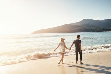 couple holding hands walking down the beach