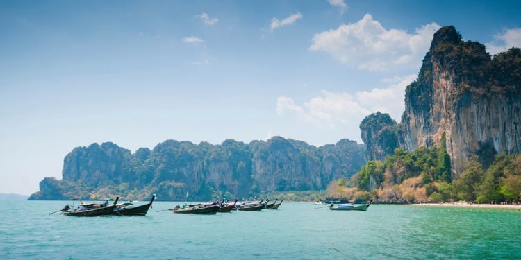 cliffs overlook boats floating on turquoise waters in thailand