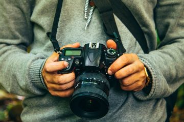 Man in a grey sweater holds a DSLR camera