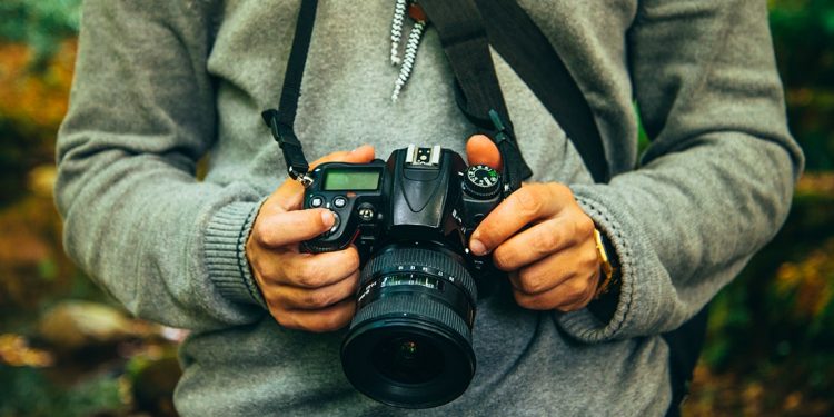 Man in a grey sweater holds a DSLR camera