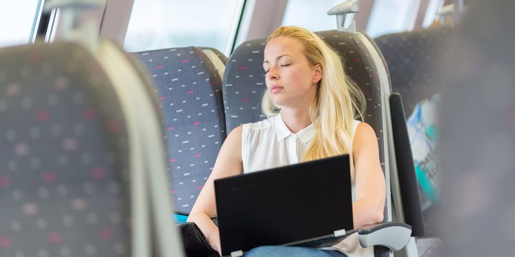 Woman with a laptop on her lap sleeps on a train