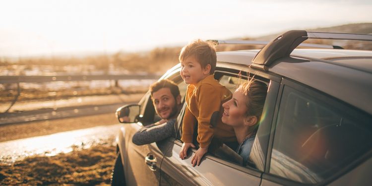 A man, woman and young child lean out the windows of a parked car