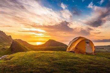 Sun rises over the water with a tent pitched on grass in the foreground