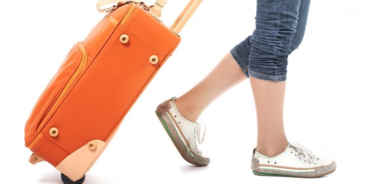 Woman in sneakers and jeans pulls an orange suitcase behind her