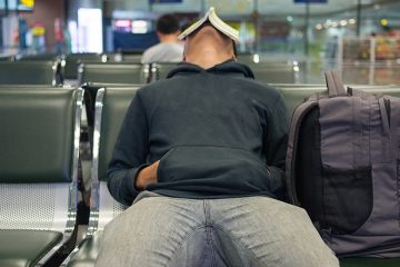 Man sleeps with a book over his face in a chair at an airport gate