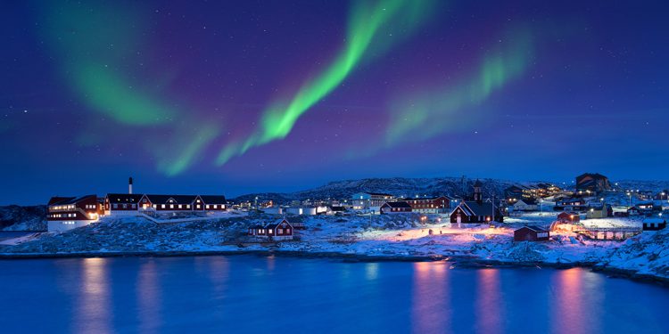 Green and pink lights of Aurora Borealis over a Greenland town at night
