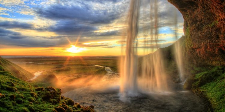 View from behind a small waterfall with the ocean and sunset in the background