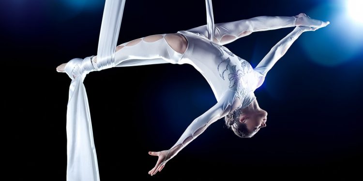 Acrobat in a white costume performs with aerial silk